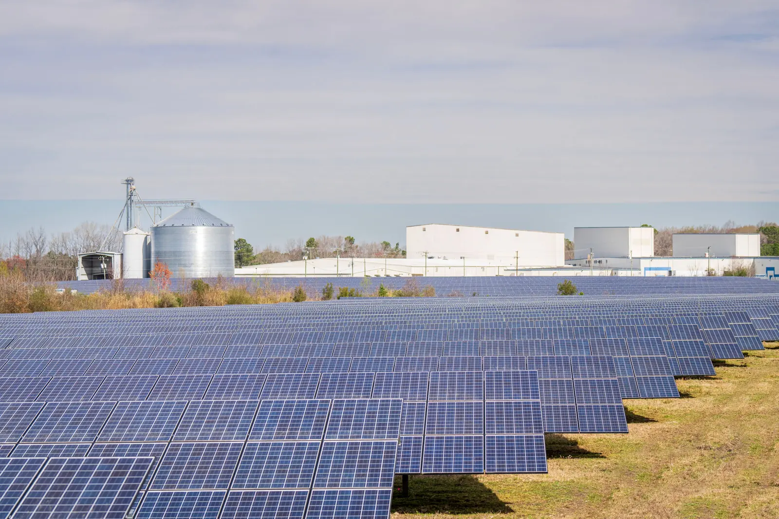 Centrale solaire au sol en plein jour, bâtiments industriels en arrière-plan